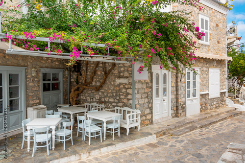 A small patio with tables and chairs in a picturesque alley of Bougainvillea flowers on the Greek Island of Hydra  Greece.