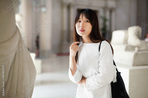 Thoughtful positive glad chinese girl in historical museum looking at antiquity art object