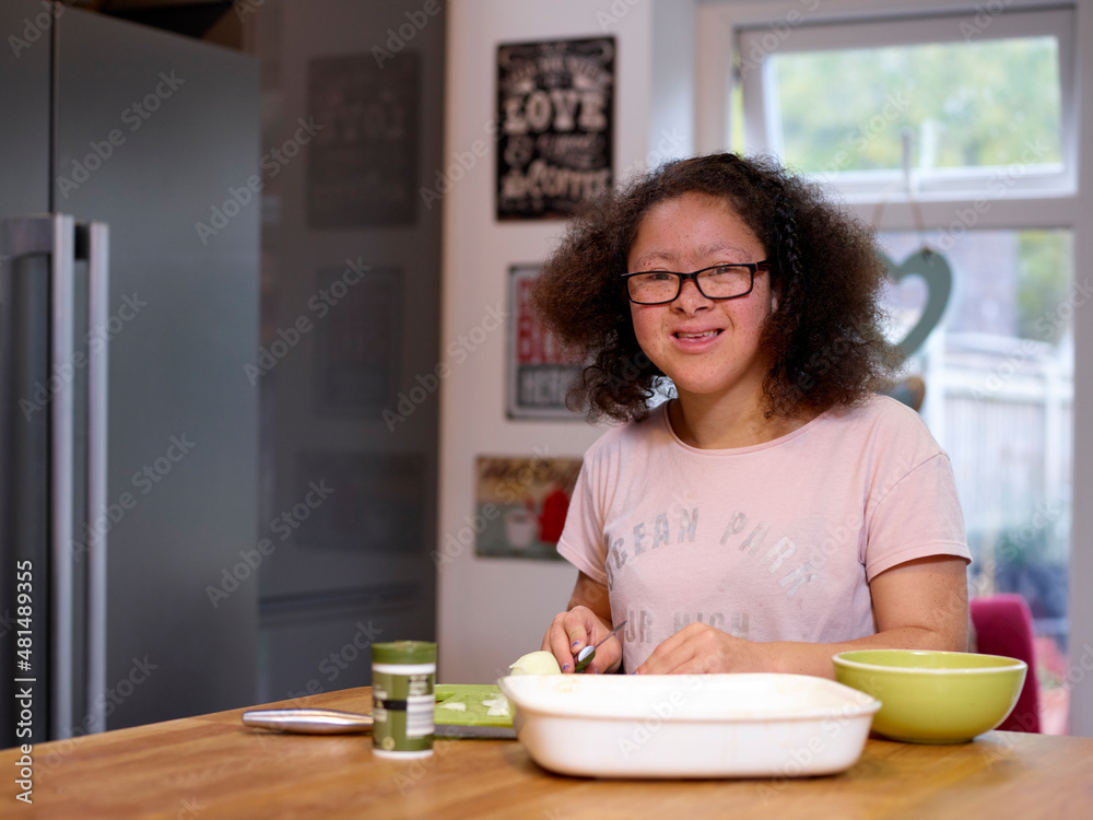 Portrait of smiling girl with Down Syndrome preparing food in kitchen Portrait of smiling girl with Down Syndrome preparing food in kitchen