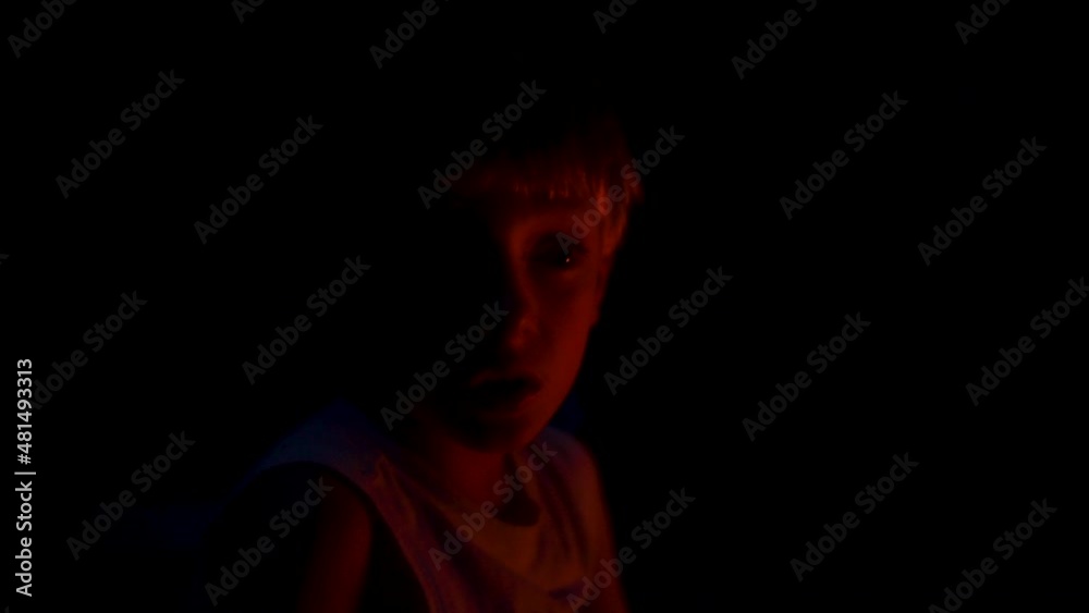 Spooky portrait of a little boy's face lit up by red firelight in the dark outdoors. Spooky portrait of a little boy's face lit up by red firelight in the dark outdoors.