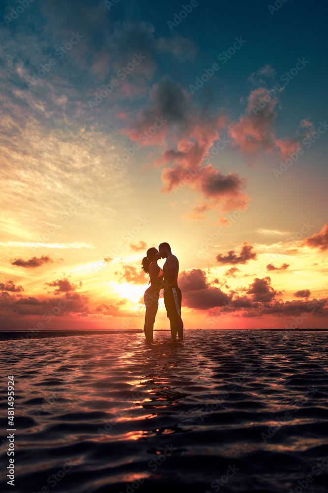 Silueta de una pareja de jóvenes enamorados besándose al amanecer en playa, contraluz