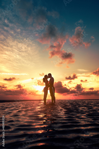 Silueta de una pareja de jóvenes enamorados besándose al amanecer en playa, contraluz