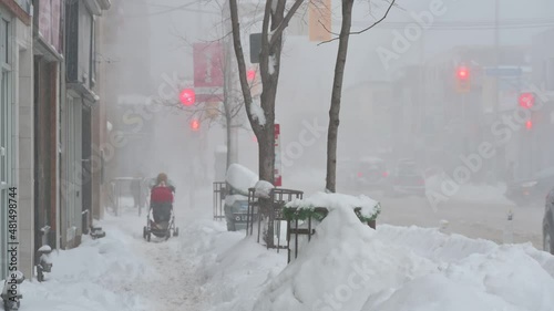 Experience the resilience of a man navigating a snowy Toronto storm with a baby carriage. snow-covered roads and sidewalks, his determination shines as he pushes through the wintry conditions.