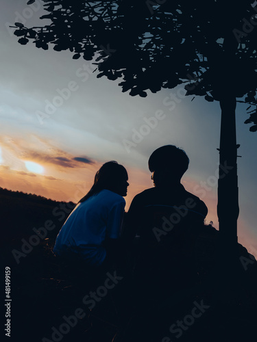 Couple man and woman in love staying under the tree with sunset scenery people romantic relationship and friendship concept.