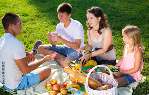 Happy young woman with her husband and two children enjoying picnic on green meadow together