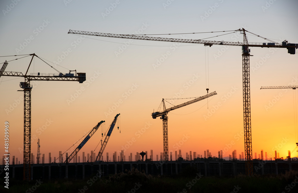 industrial construction cranes and building silhouettes over the sun at sunrise
