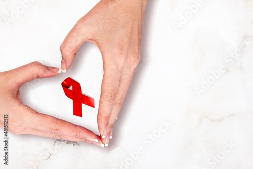 Female hands with red ribbon symbol of aids awareness on background