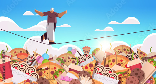 senior woman balancing on rope above junk food assortment of fast food unhealthy nutrition junkfood addiction