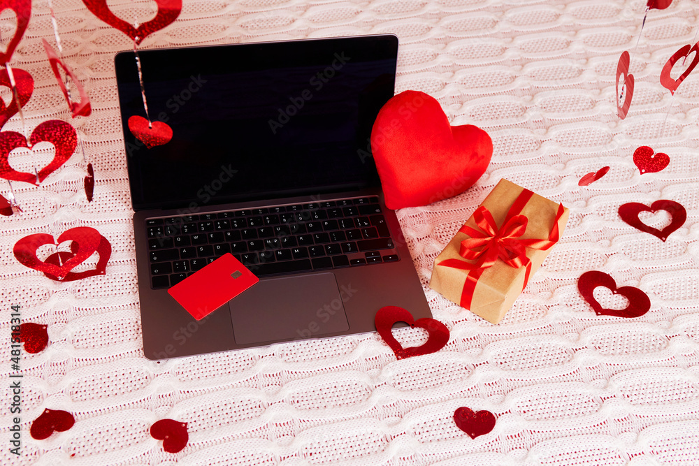 Laptop, credit card, gift, decor, hearts on a white knitted blanket. Shopping online for Valentine's Day. Mock up