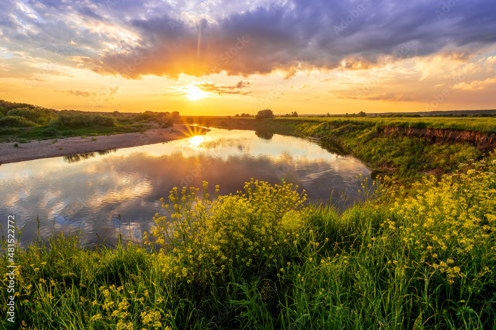 Amazing view at beautiful sunset or sunrise on a shiny lake from hill with green bushes, golden sun rays, calm water ,deep blue cloudy sky and forest on a background Amazing view at beautiful sunset or sunrise on a shiny lake from hill with green bushes, golden sun rays, calm water ,deep blue cloudy sky and forest on a background