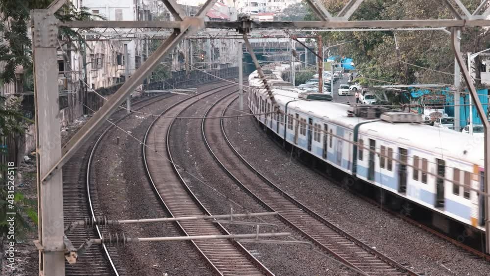Real Time video of Mumbai Local Train honking and passing by a foot over bridge. Wide angle view of Rail tracks and Western Railway Passenger Train commuting during evening. Mumbai, Maharashtra, India