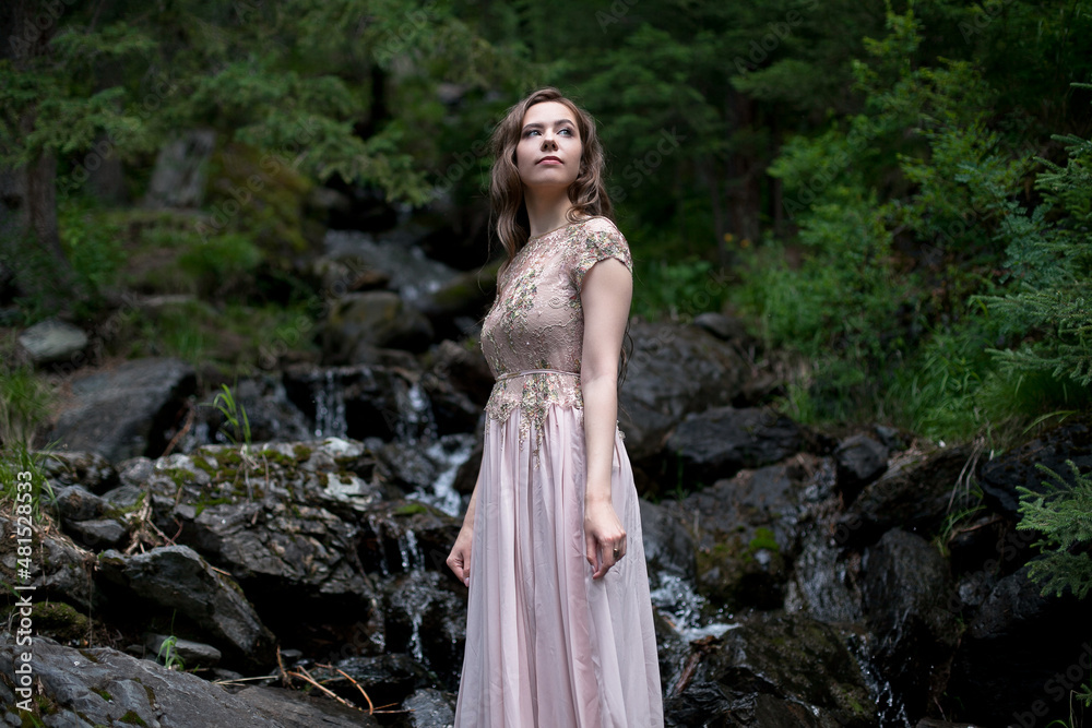 A young woman in a long dress on the background of a mountain waterfall. Enjoyment of nature. A young woman in a long dress on the background of a mountain waterfall. Enjoyment of nature.