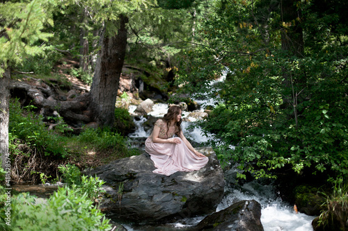 A young woman in a long dress on the background of a mountain waterfall. Enjoyment of nature.