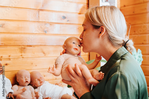 Billede på lærred Portrait pretty caucasian young woman kissing realistic newborn baby doll sittin