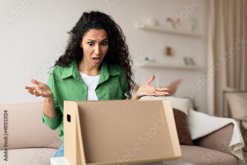 Discontented Female Customer Unpacking Cardboard Box At Home
