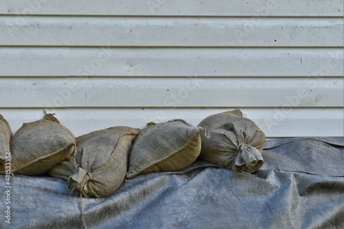 Dirty white house wall with row of sandbags on black tarp.  Room for copy. photo