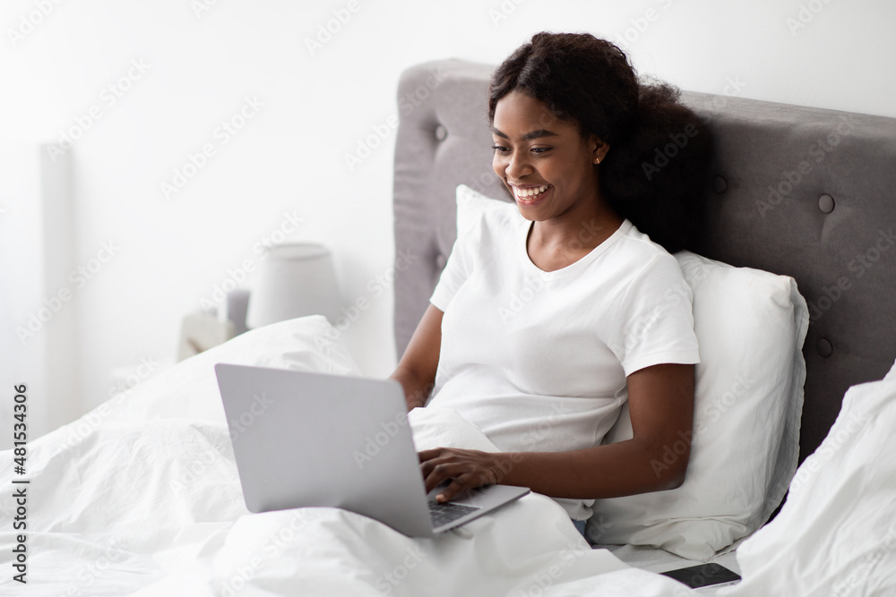 Cheerful african american lady independent contractor using notebook in bed Cheerful african american lady independent contractor using notebook in bed