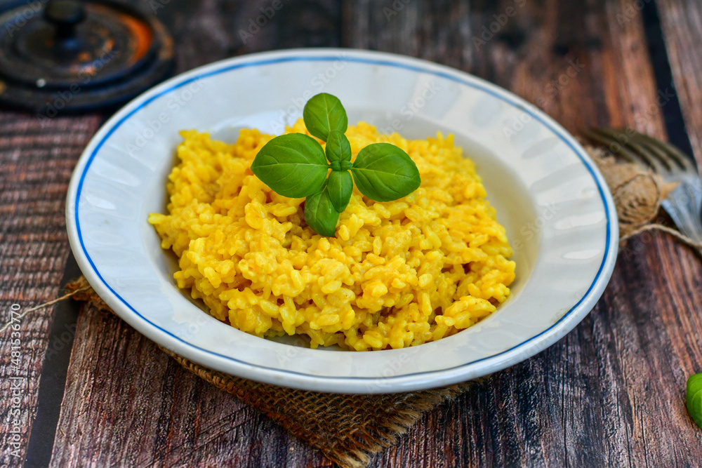 Italian creamy risotto milanese with parmesan cheese and fresh basil on rustic background Italian creamy risotto milanese with parmesan cheese and fresh basil on rustic background