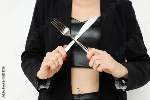 photo pretty woman in a black jacket a knife and a fork near the face light background