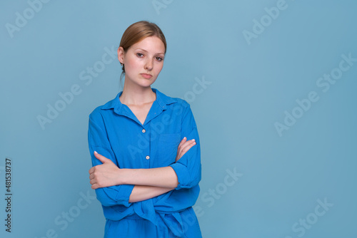 Photo portrait young female expert with folded hands, wearing blue shirt, with a contemplative expression, standing next to an empty space, isolated on a pastel blue background.