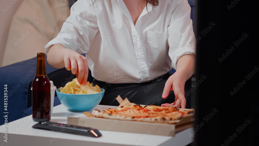 Close up of woman placing box of pizza on table while having beverages and bowl of chips. Caucasian person preparing to eat takeaway meal from fast food restaurant in living room