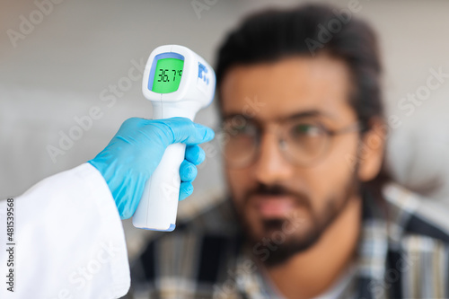 Nurse hand with thermometer against arab guy forehead