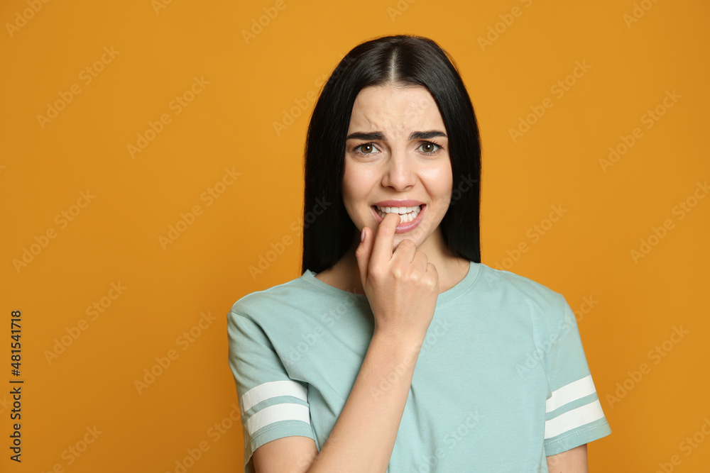 Young woman biting her nails on yellow background Young woman biting her nails on yellow background