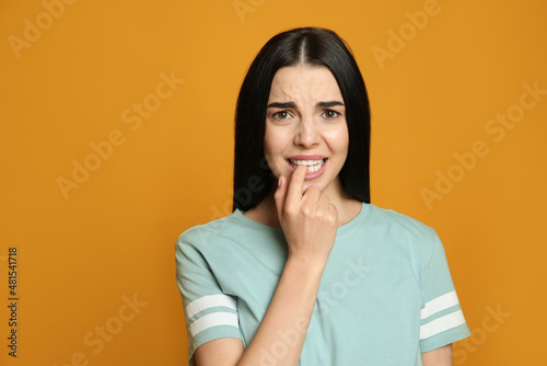 Young woman biting her nails on yellow background