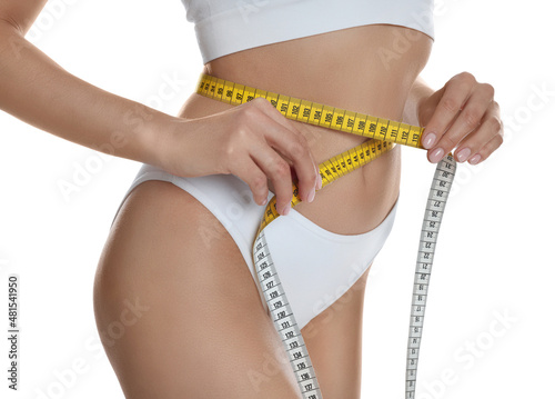 Young woman measuring waist with tape on white background, closeup
