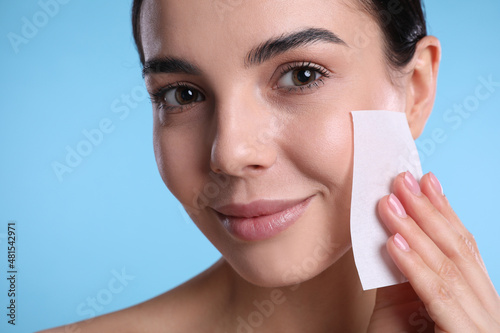 Canvas Print Beautiful woman using mattifying wipe on light blue background, closeup