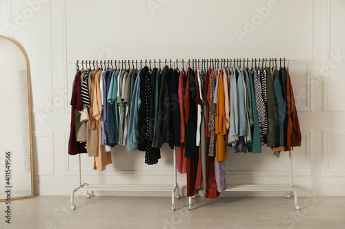 Racks with stylish clothes and mirror near white wall indoors. Fast fashion