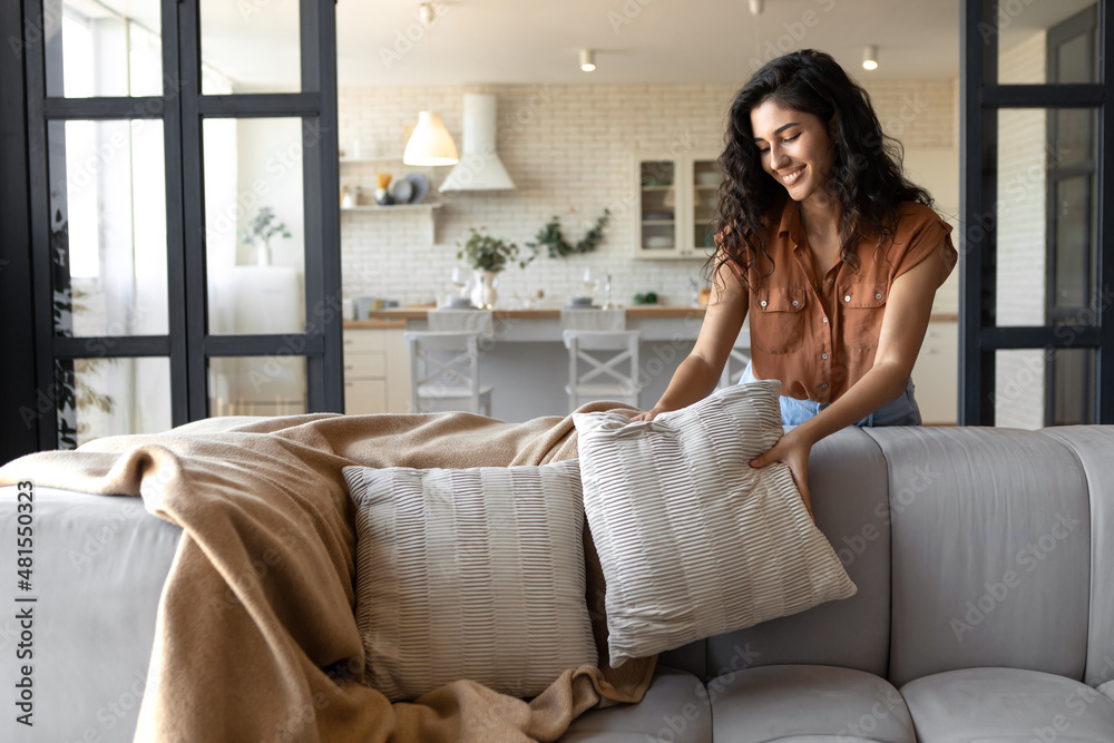 Lovely young woman putting soft pillows and plaid on comfy sofa, making her  home cozy and warm, copy space Photos | Adobe Stock