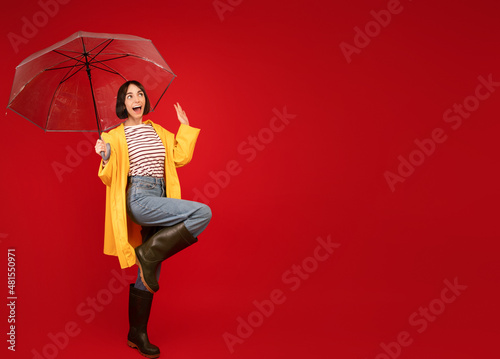 Autumn sales concept. Portrait of surprised lady standing under umbrella and looking at free space, red background photo