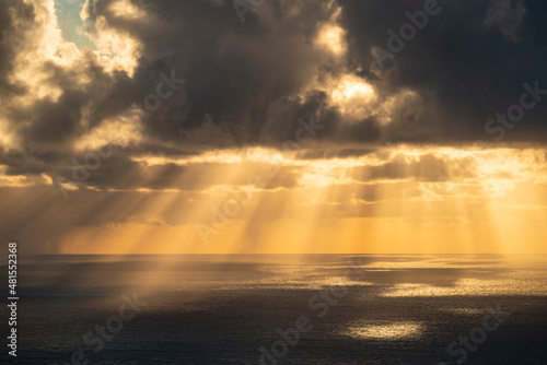 Beautiful cloudscape over the Atlantic Ocean on the coast of Madeira at sunset. Warm yellow sun rays penetrate the clouds and shine on the dark water surface.