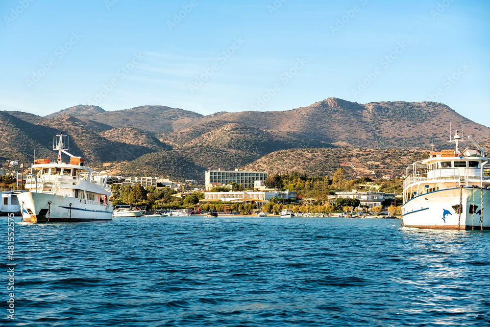 View to the shoreline with moored ships. Houses and mountain range at the blurred background. 