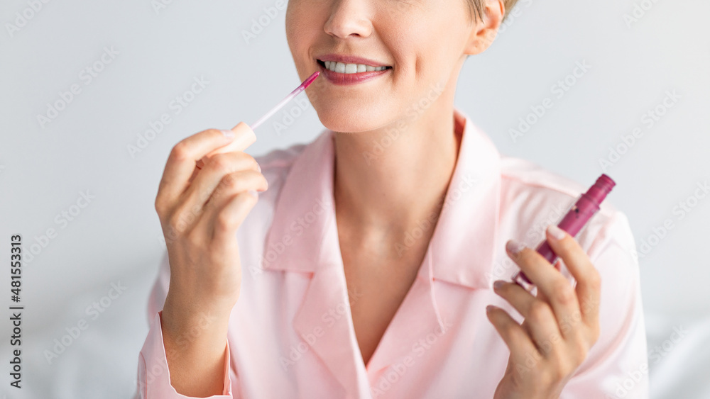 Smiling woman holding lip gloss and holding tube Smiling woman holding lip gloss and holding tube