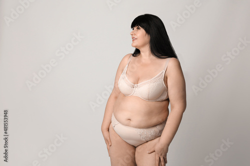 Beautiful overweight woman in beige underwear on light background, space for text. Plus-size model
