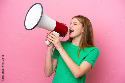 Teenager Russian girl isolated on pink background shouting through a megaphone to announce something in lateral position