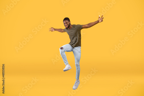Happy african american guy jumping up over yellow background, full-length portrait, free space