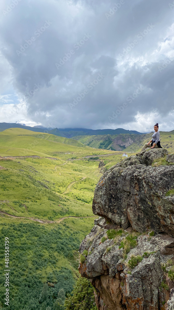 A girl sitting on top of a rock against the backdrop of mountain landscapes in the Elbrus region, Kabardino-Balkaria