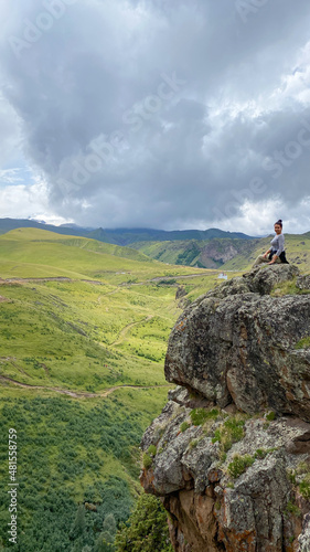 A girl sitting on top of a rock against the backdrop of mountain landscapes in the Elbrus region  Kabardino-Balkaria