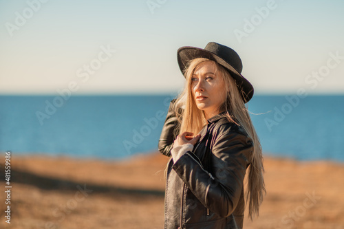 A blonde in a stylish black leather jacket walks along the seashore.