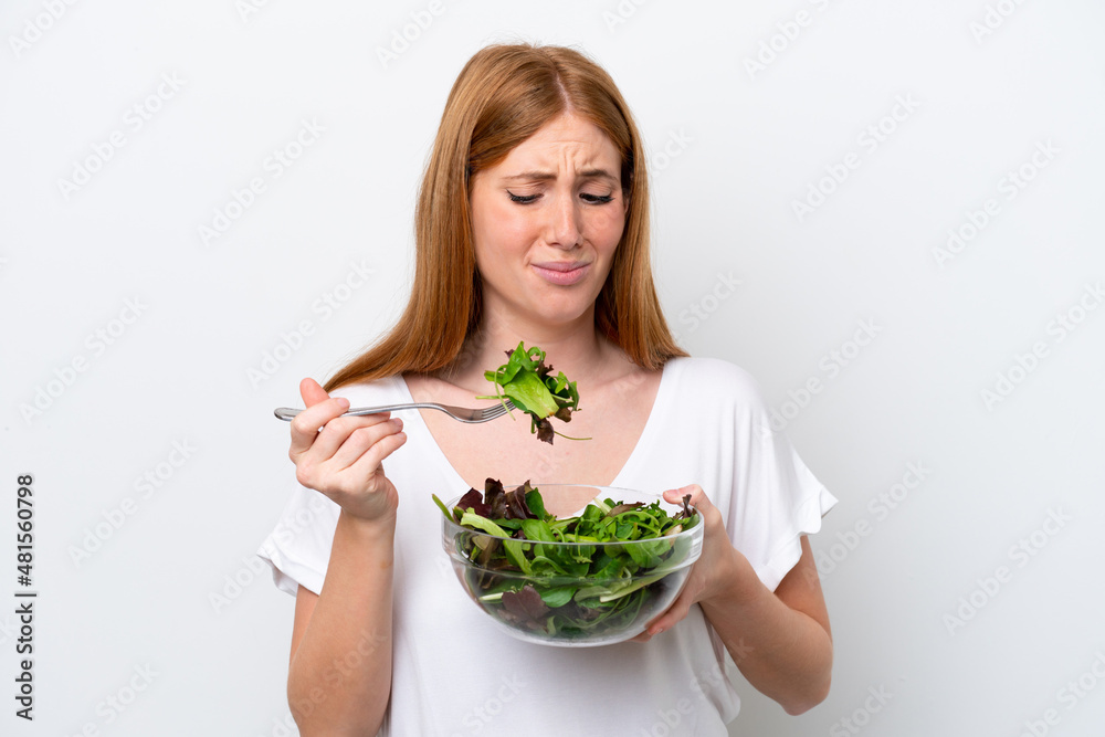 Young redhead woman isolated on white background holding a bowl of salad with sad expression Young redhead woman isolated on white background holding a bowl of salad with sad expression