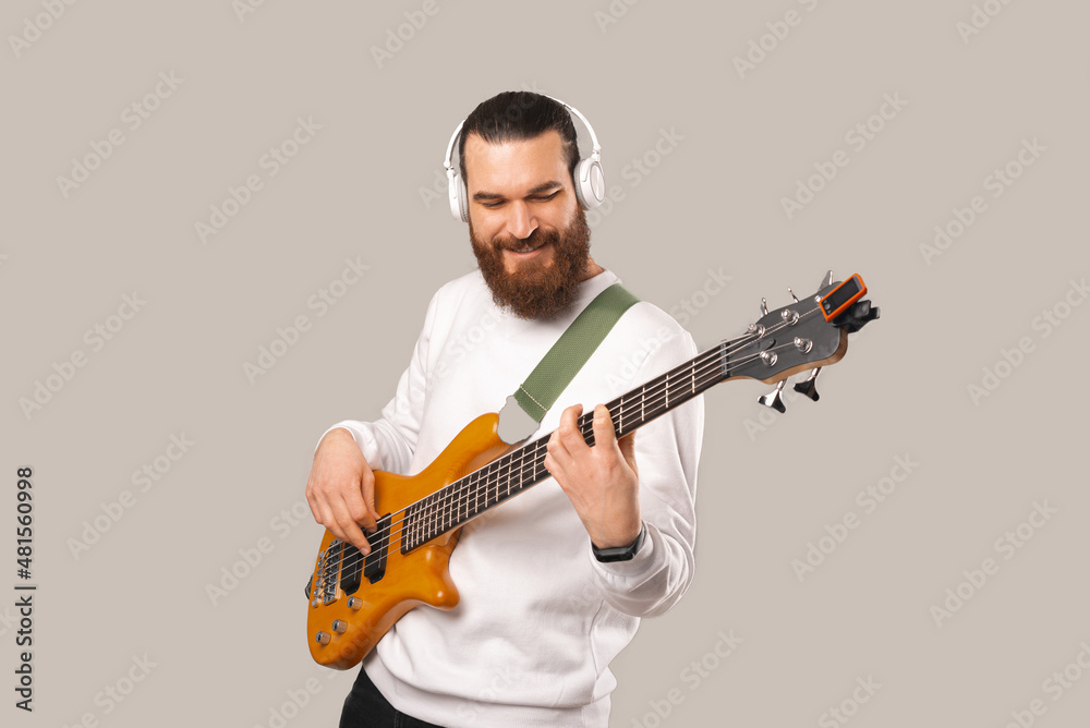 Photo of young handsome bearded man playing at bass guitar with 5 strings. Photo of young handsome bearded man playing at bass guitar with 5 strings.