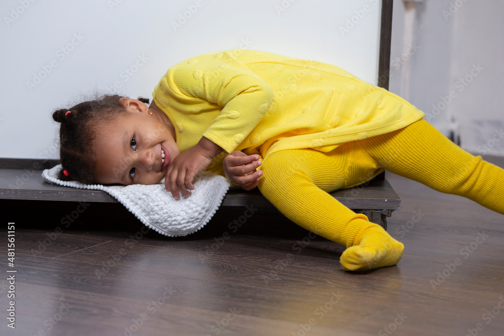 A little African American girl in a yellow dress lies on the floor and smiles. A little African American girl in a yellow dress lies on the floor and smiles.