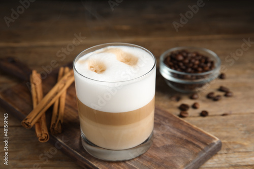 Delicious latte macchiato, cinnamon sticks and coffee beans on wooden table