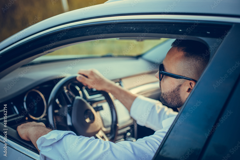 Portrait of an handsome guy driving his car. Bearded man of style and status. Handsome young man in full suit smiling while driving a white luxury car. Portrait of an handsome guy driving his car. Bearded man of style and status. Handsome young man in full suit smiling while driving a white luxury car.