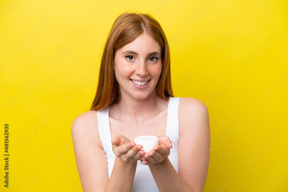 Young redhead woman isolated on yellow background with moisturizer and offering it Young redhead woman isolated on yellow background with moisturizer and offering it