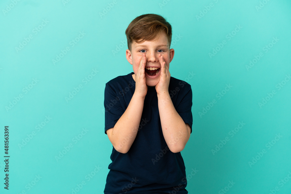 Little redhead boy isolated on blue background shouting and announcing something Little redhead boy isolated on blue background shouting and announcing something