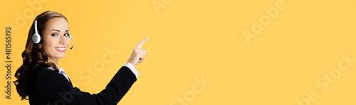 Call Center Service. Customer support or sales agent. Businesswoman or caller or phone operator in black suit showing pointing at copy space. Orange yellow background. Help answering, consulting.